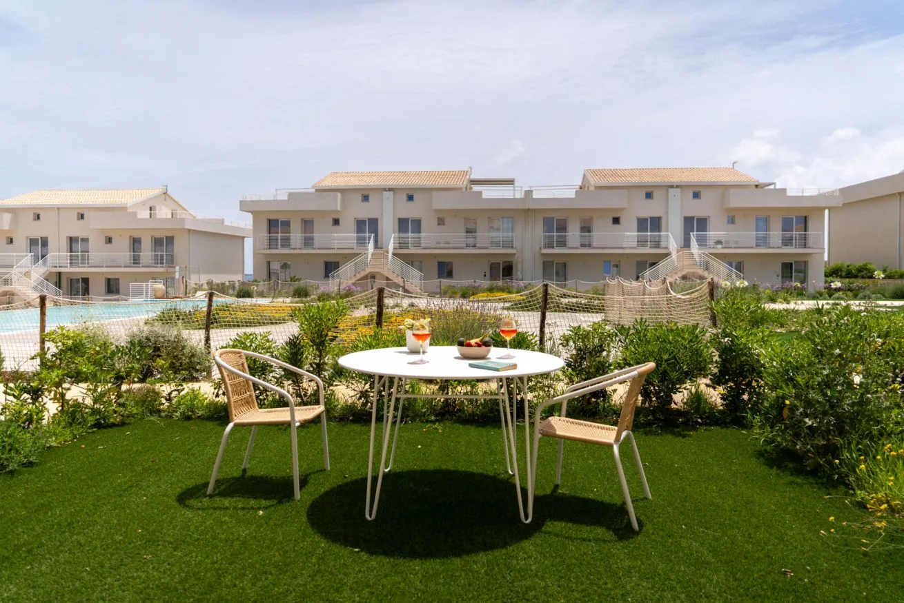 A garden patio has a round table and seating in front of modern apartment buildings.