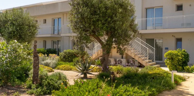 A landscaped garden with trees and shrubs fronts a building with balconies and exterior stairs.