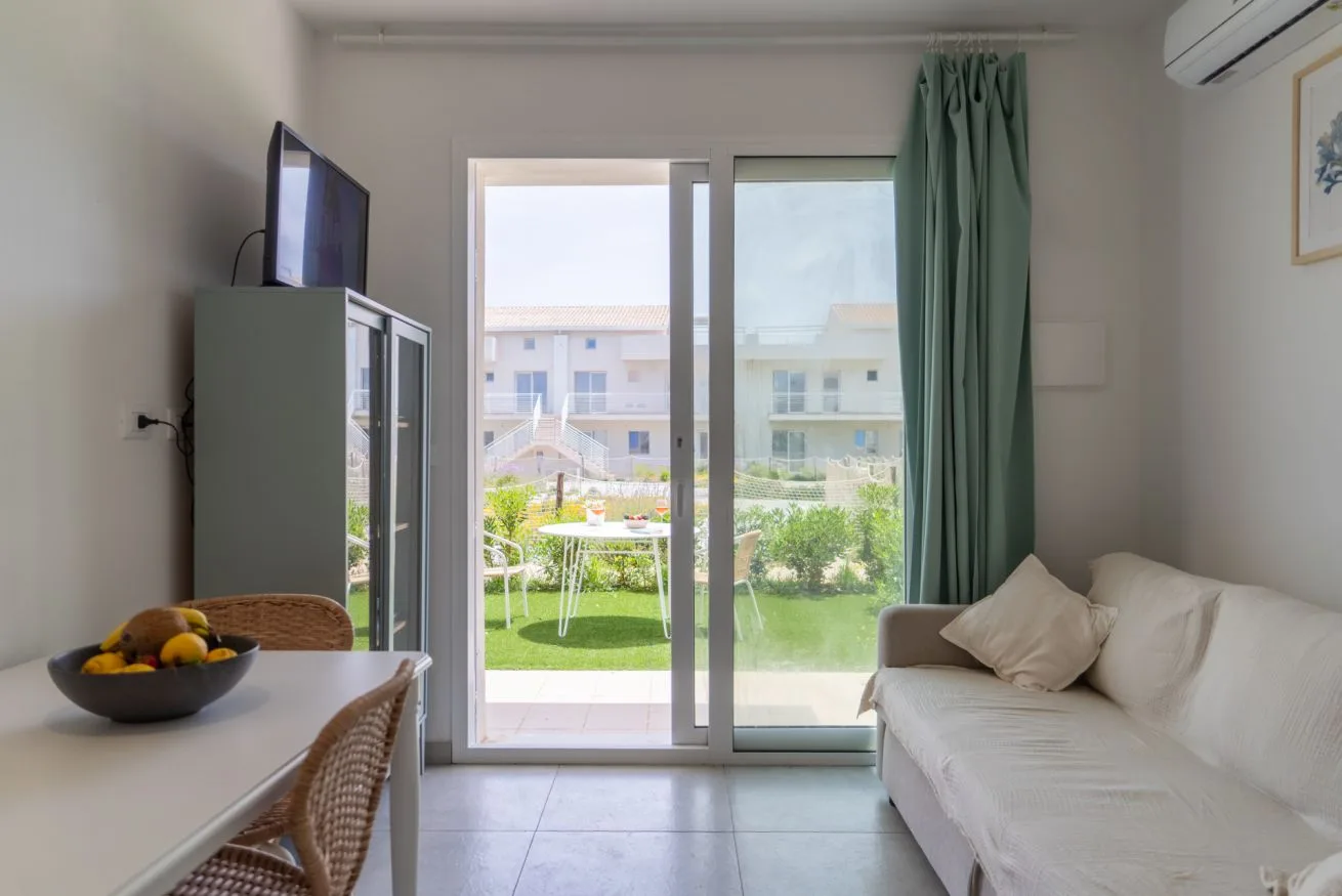 Living room with white seating beside glass doors opening onto a garden.