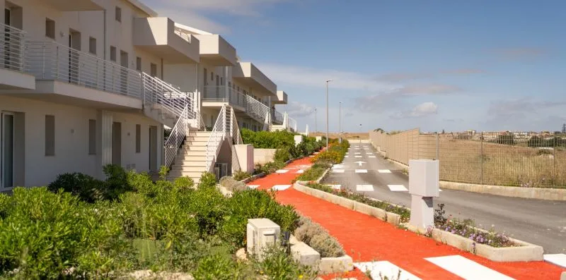 A row of modern buildings overlooks a red pedestrian path and paved roadway.