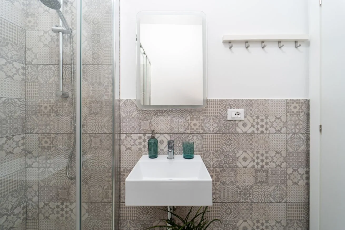 A bathroom with a wall-mounted sink, mirror, and tiled walls.