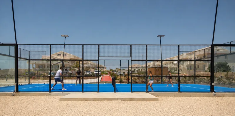 An outdoor padel court with players behind a wire fence.
