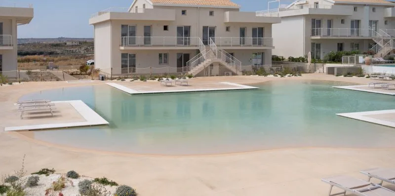 A swimming pool sits in front of a modern multi-story building.