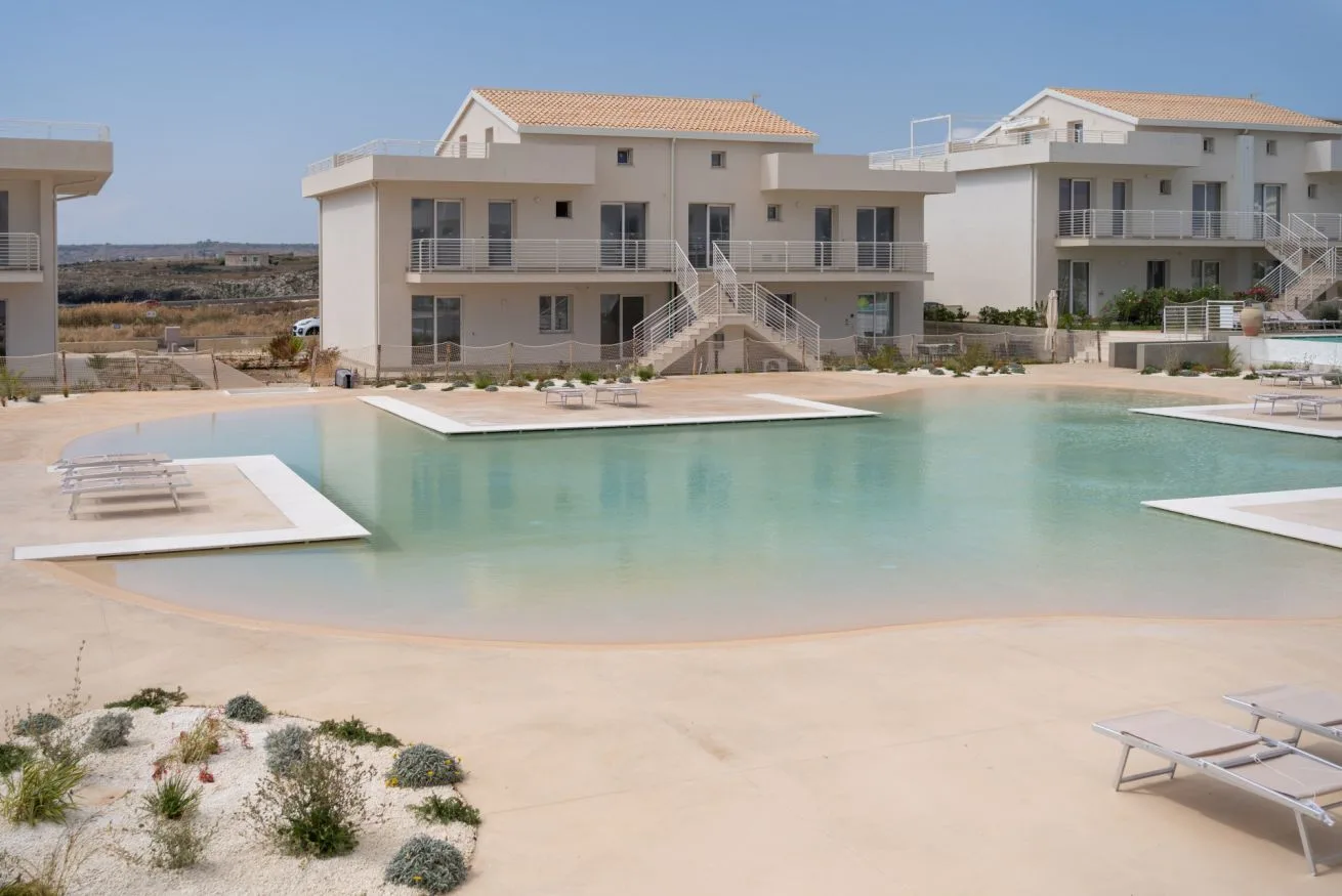 A large outdoor swimming pool sits in front of modern apartment buildings.