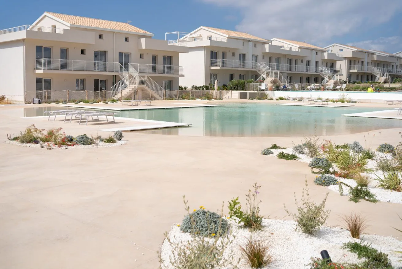 A landscaped swimming pool sits in front of a row of modern residential buildings.