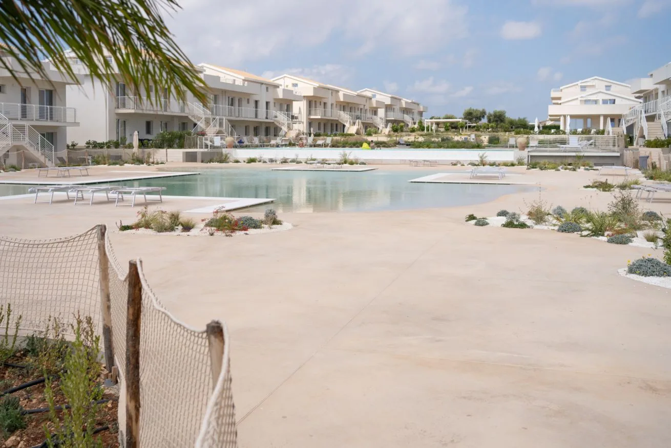 A shallow outdoor pool sits among pale buildings and landscaped paths.