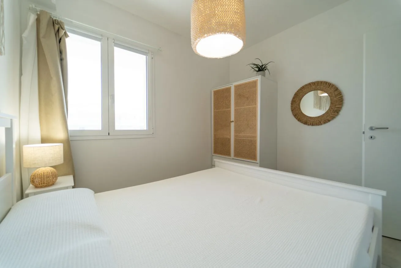 A bright bedroom with a large bed, window, and woven pendant light.