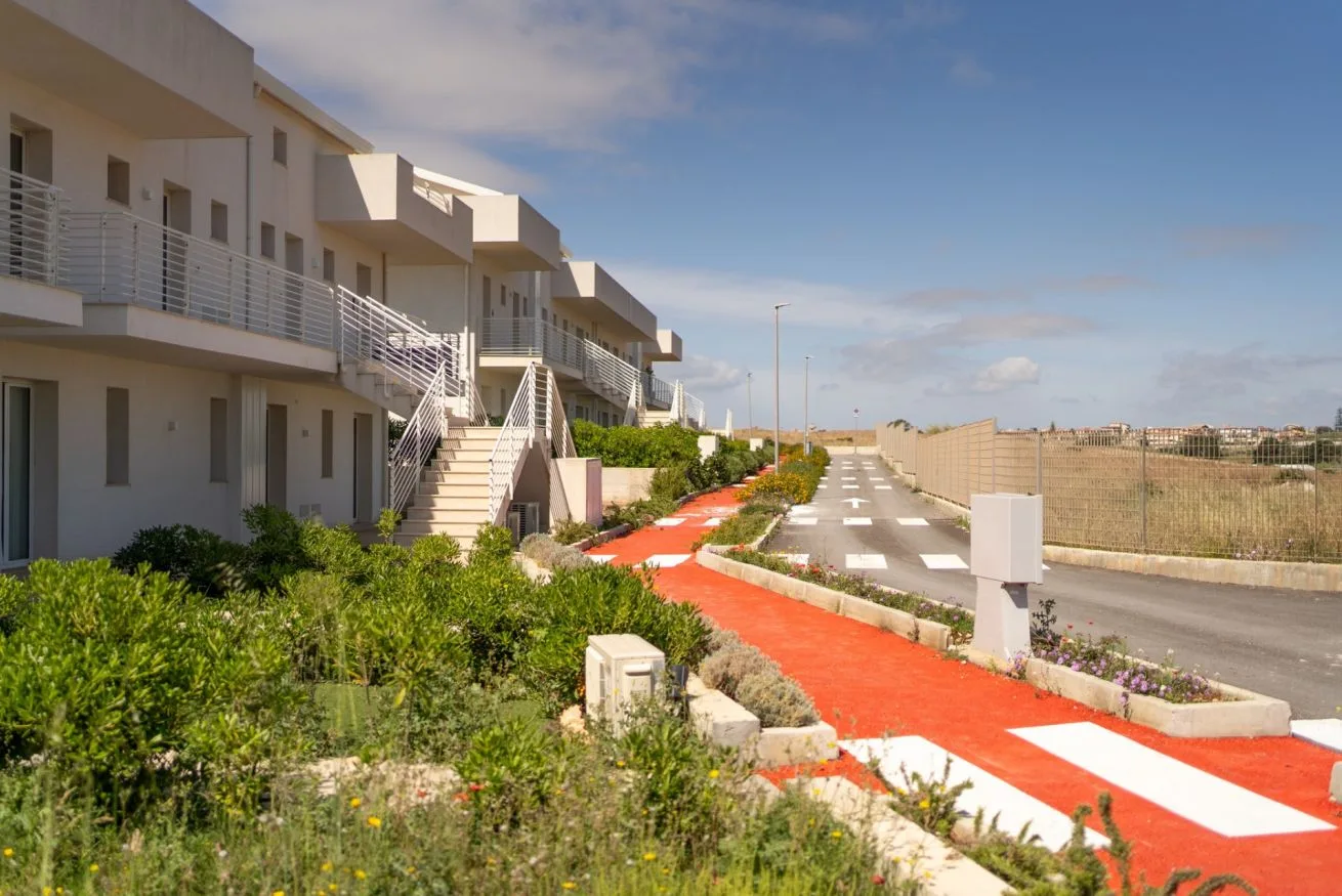 A row of modern buildings overlooks a red pedestrian path and parking area.