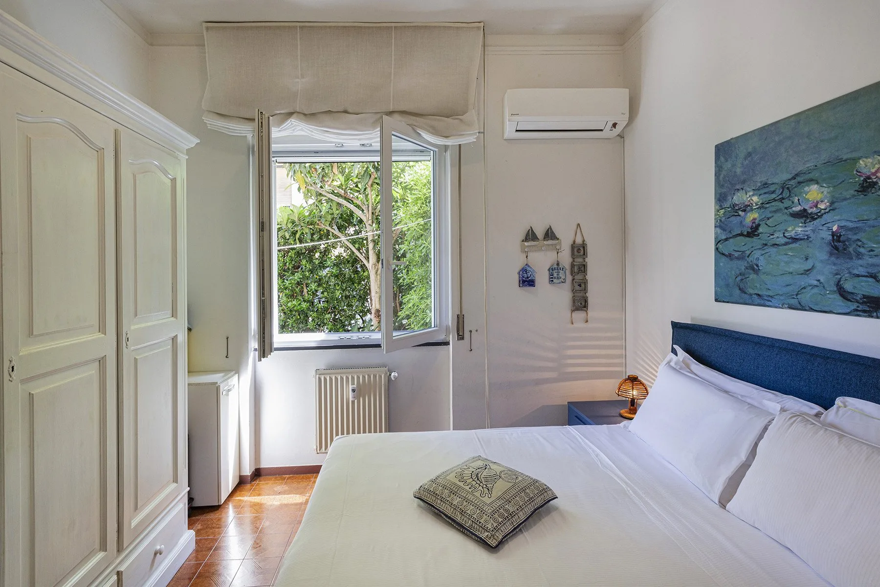 Un dormitorio luminoso con una cama bien tendida junto a una ventana con vegetación.