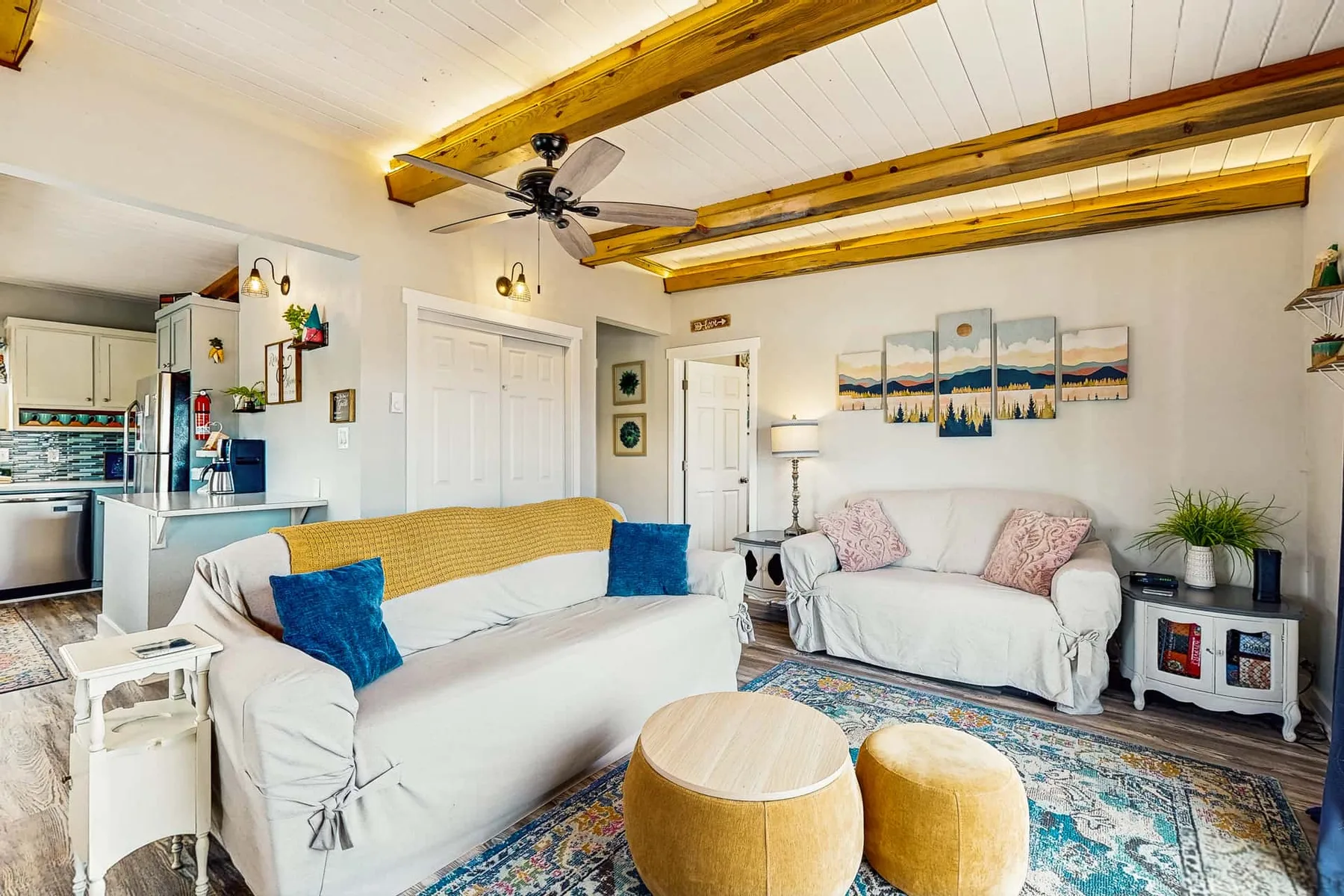A living room with light-colored seating, a patterned rug, and exposed ceiling beams.