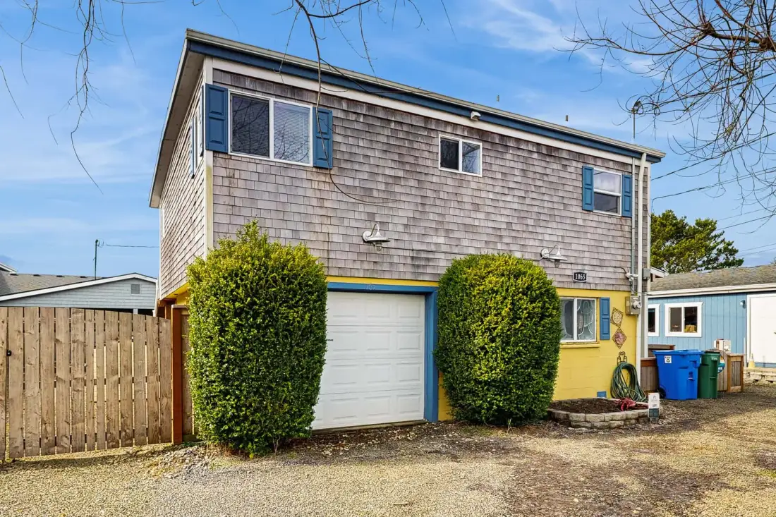A two-story house with shingle siding, a garage, and trimmed shrubs.