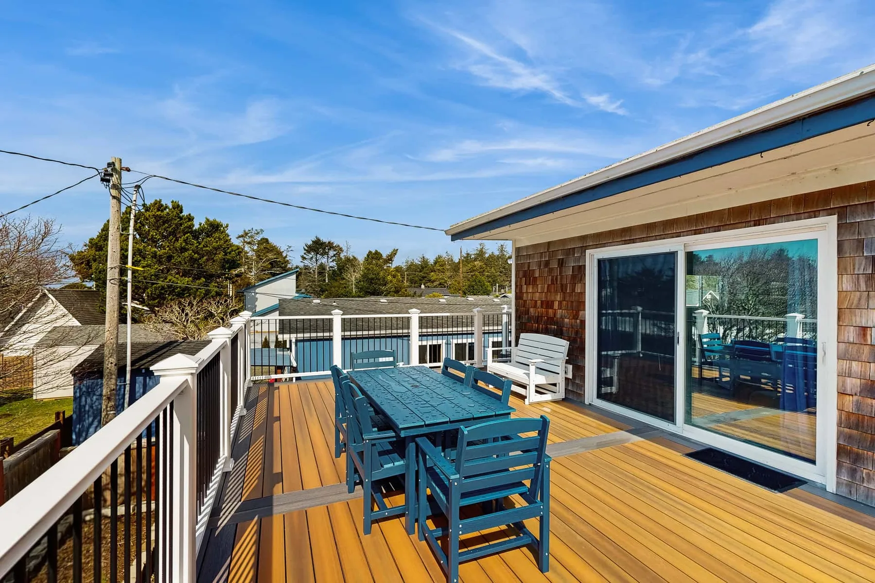An outdoor deck has blue dining furniture beside a building with sliding glass doors.
