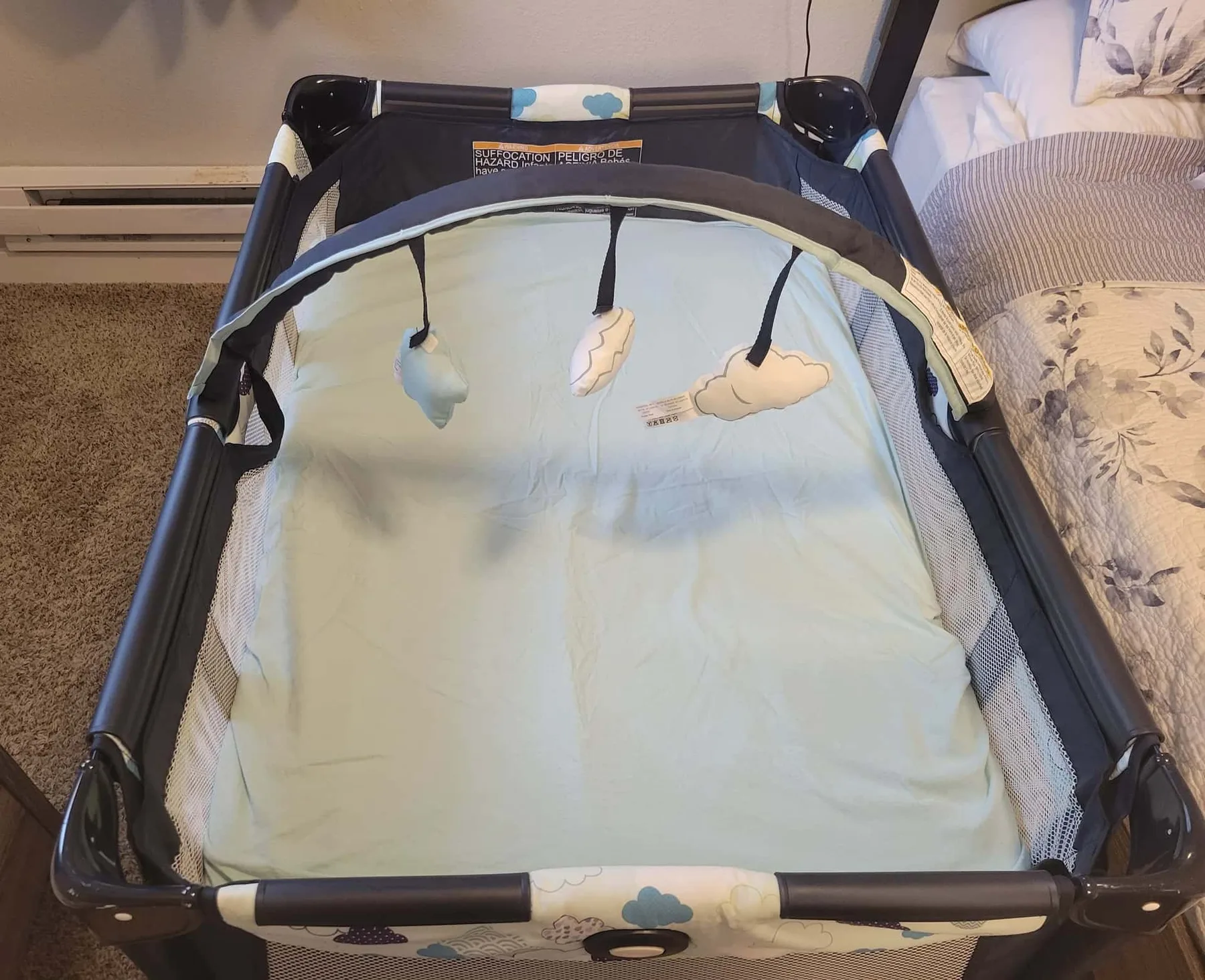 A portable baby play yard with a padded floor and hanging toys.