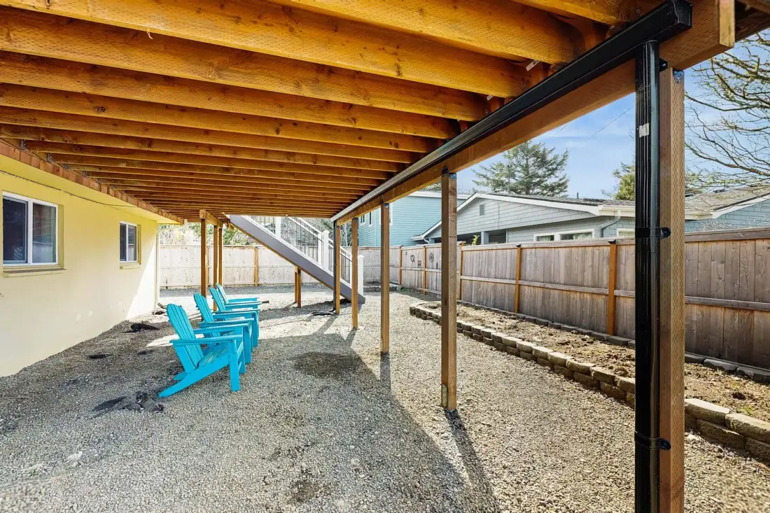A covered outdoor seating area with turquoise chairs beside a fenced yard.