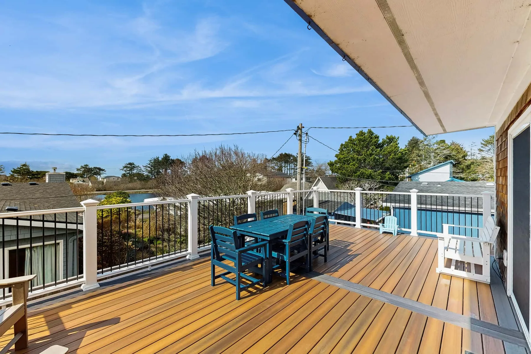 A sunny outdoor deck with blue seating and a railing overlooks nearby rooftops.
