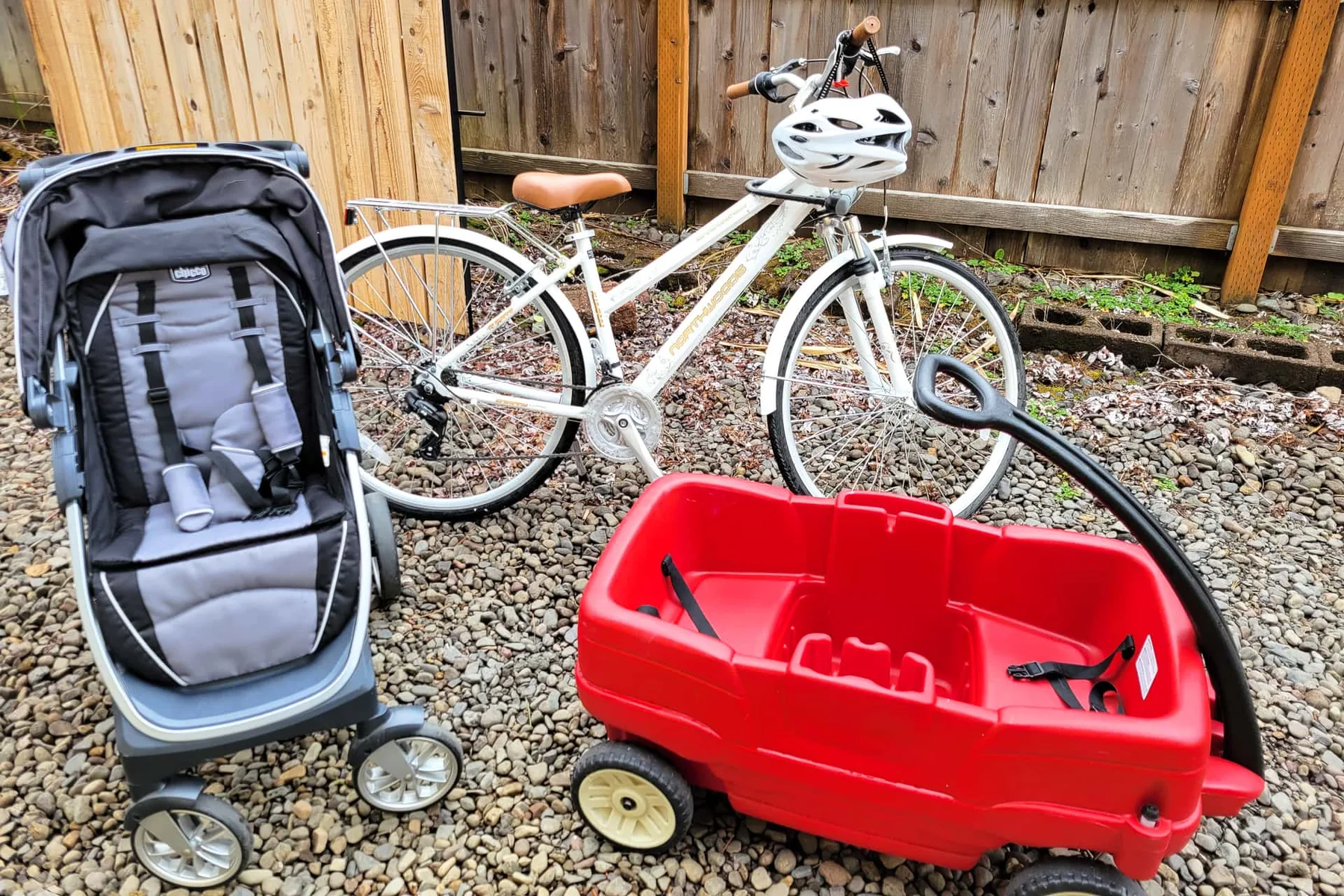A gravel yard with a stroller, bicycle, and red wagon.