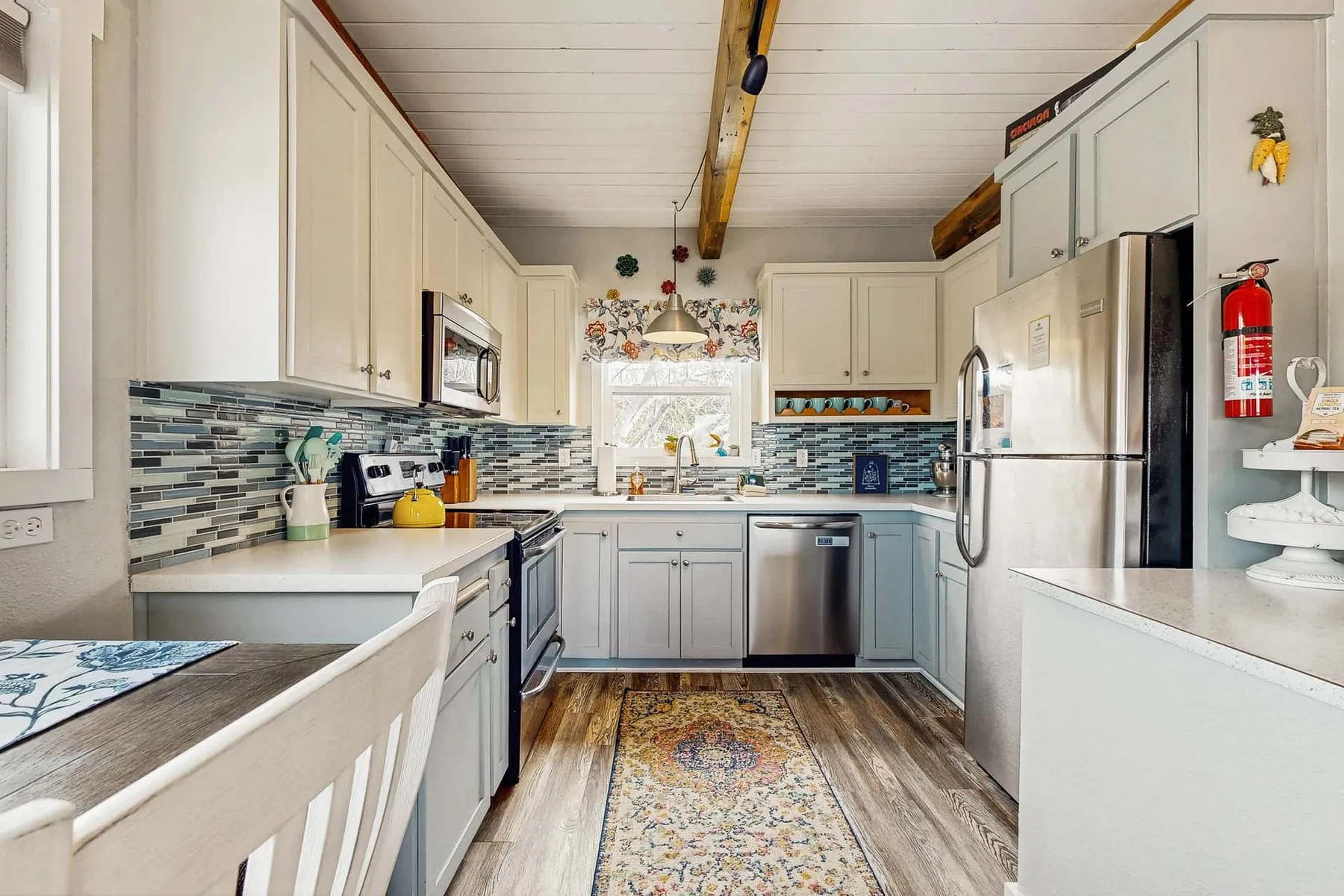 A bright kitchen with pale cabinets, tiled backsplash, and stainless steel appliances.