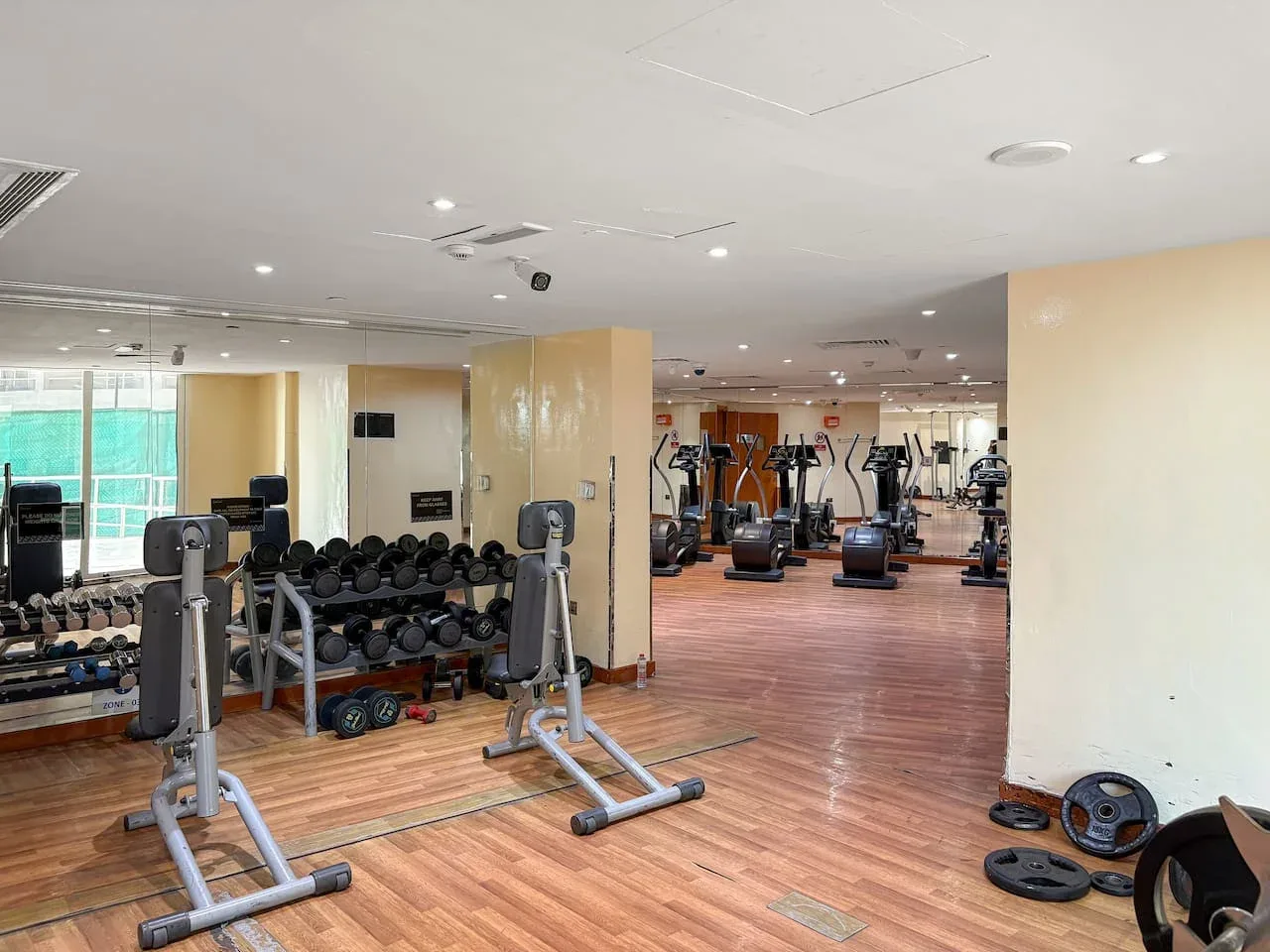 A gym with exercise machines and weights arranged across a wood-floored room.