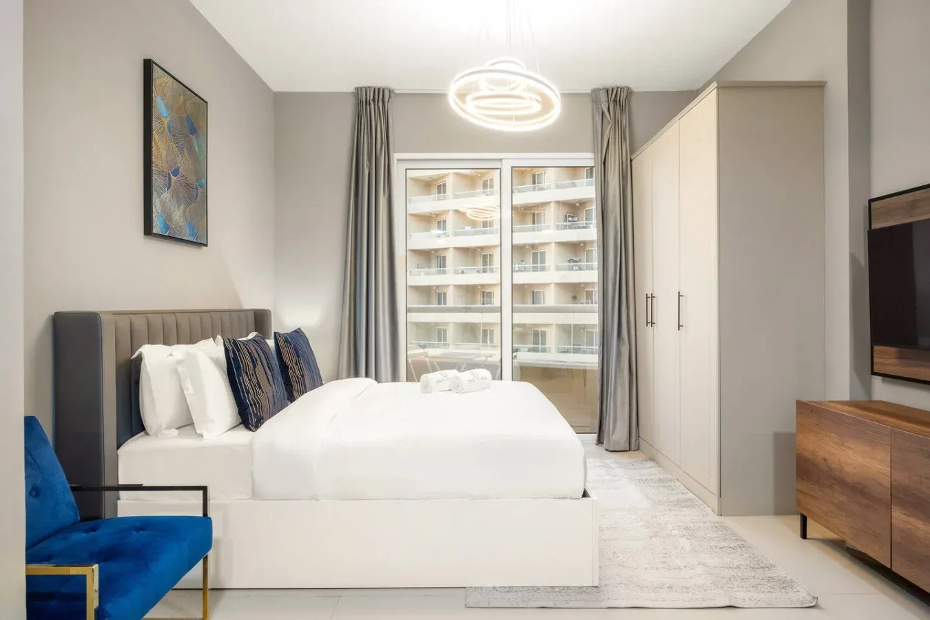 A bright bedroom with a large bed, a wardrobe, and a window.