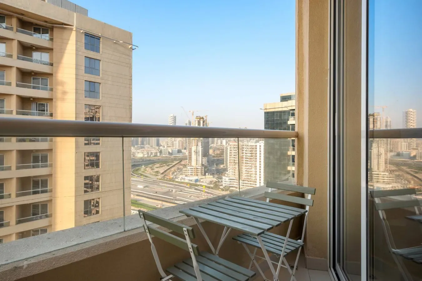 A balcony with a small table and chairs overlooking city buildings and roads.