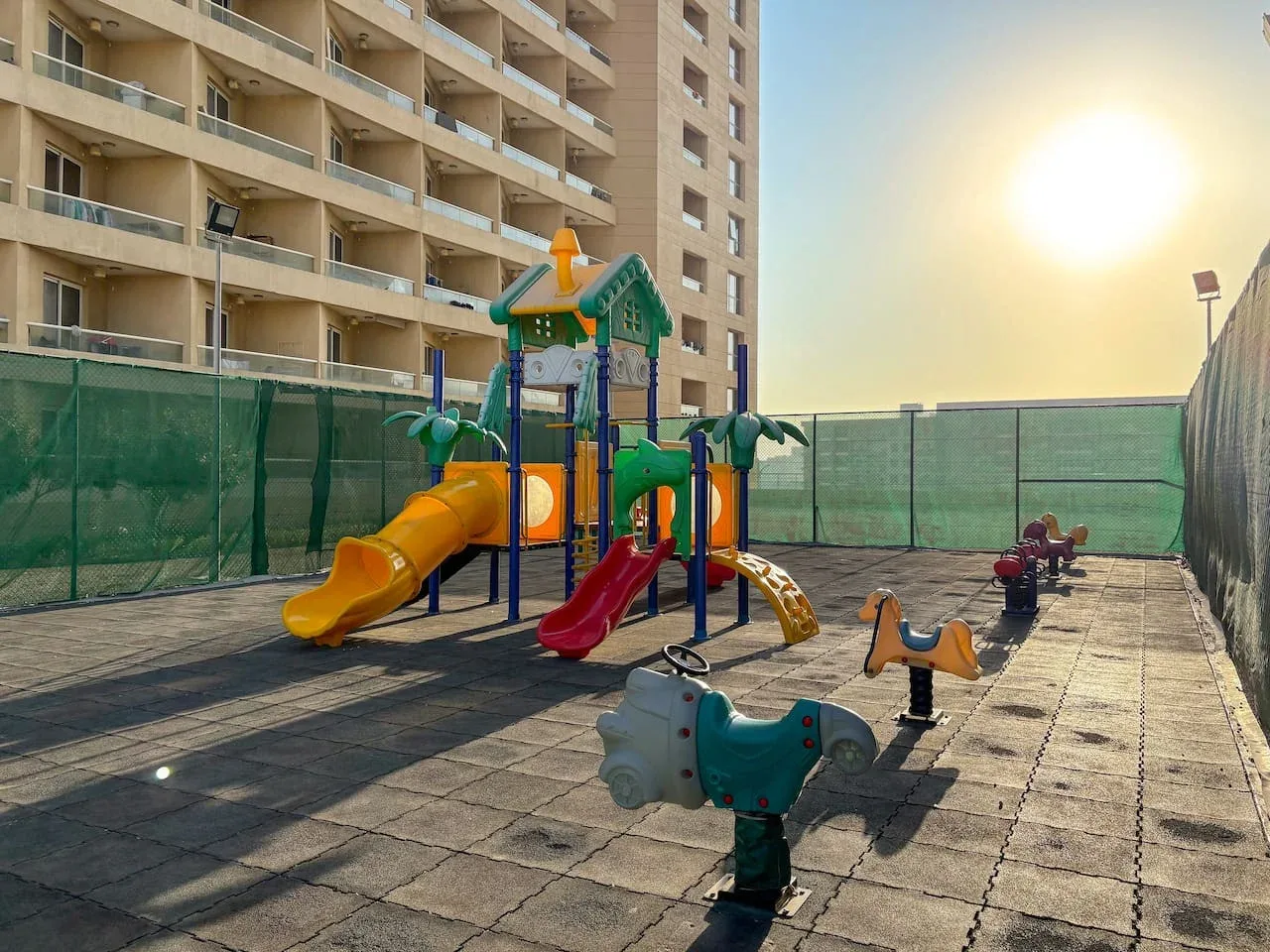 An outdoor playground with colorful slides and spring riders sits beside a residential building.
