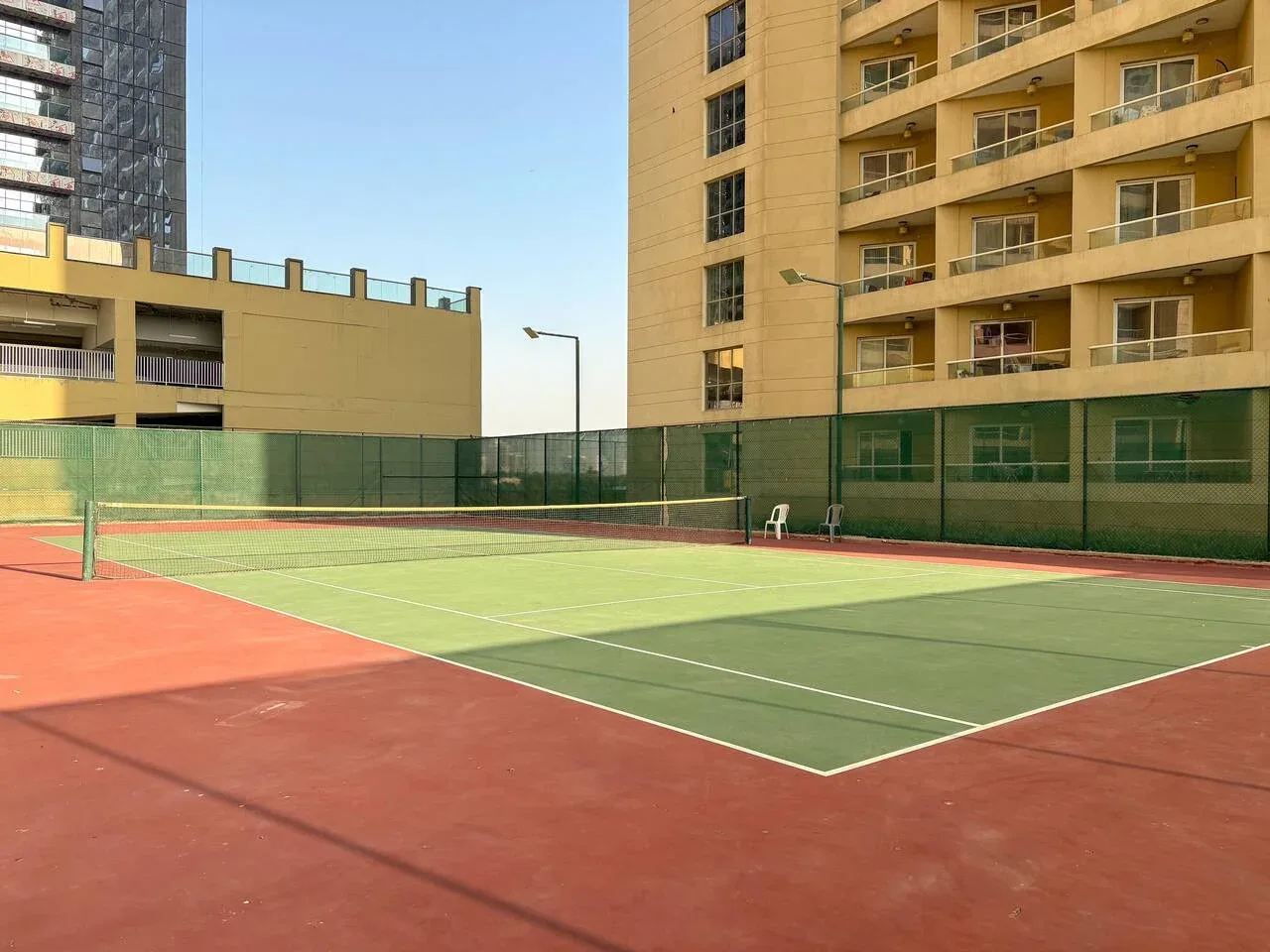 An outdoor tennis court with a net, surrounded by apartment buildings.