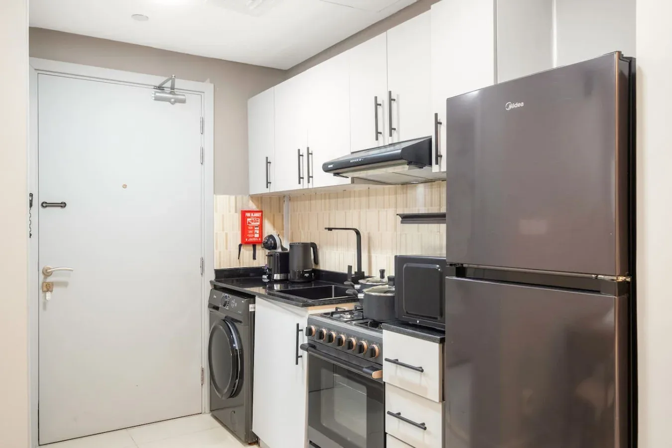 A compact kitchen with white cabinets, a refrigerator, and cooking appliances.