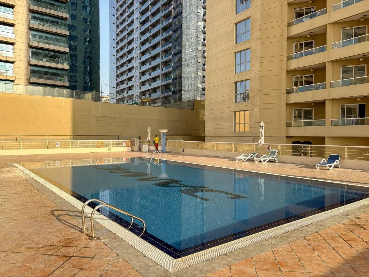 An outdoor swimming pool sits among tall apartment buildings.