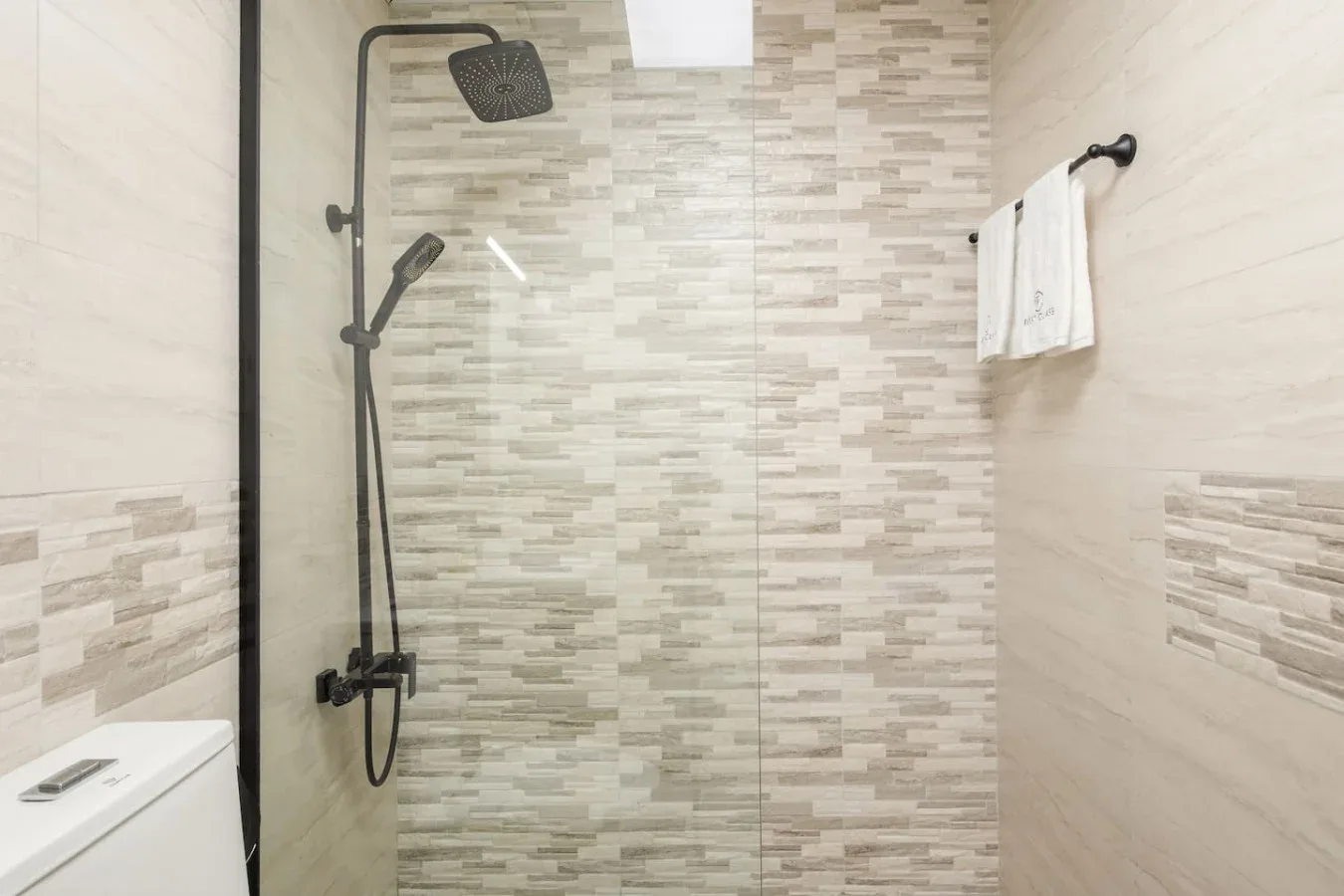 A tiled bathroom shower with dark fixtures and a towel on the wall.