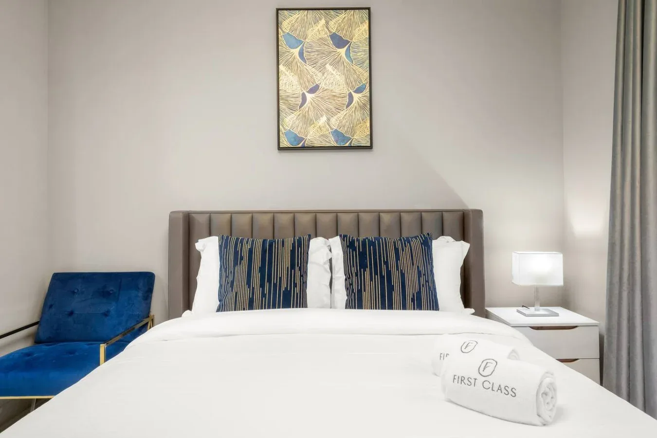 A bedroom with a neatly made bed, patterned pillows, and a blue armchair.