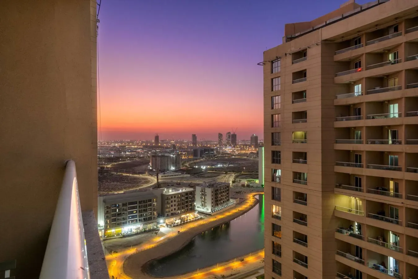 City buildings and a winding canal glow beneath a colorful sunset sky.