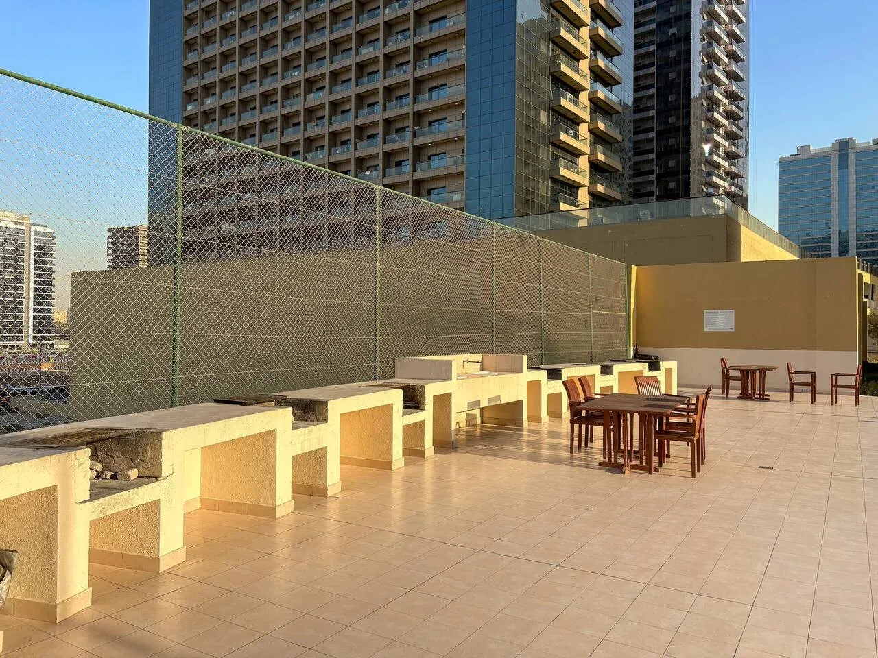 An outdoor rooftop patio has tiled flooring, tables, and surrounding high-rise buildings.