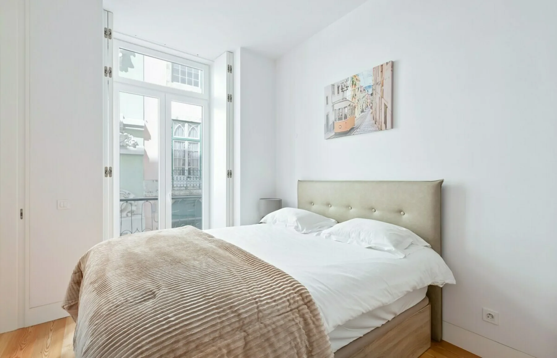 A bright bedroom with a double bed beside tall windows.