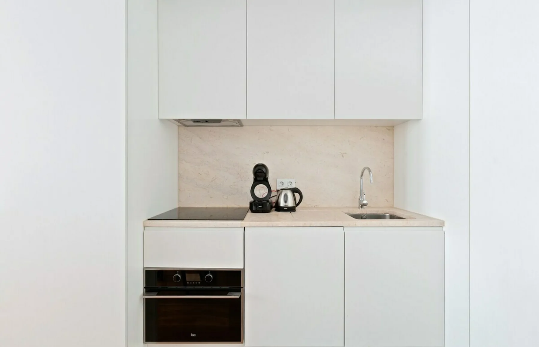 Una cocina compacta con armarios blancos, una placa de cocción y un fregadero.