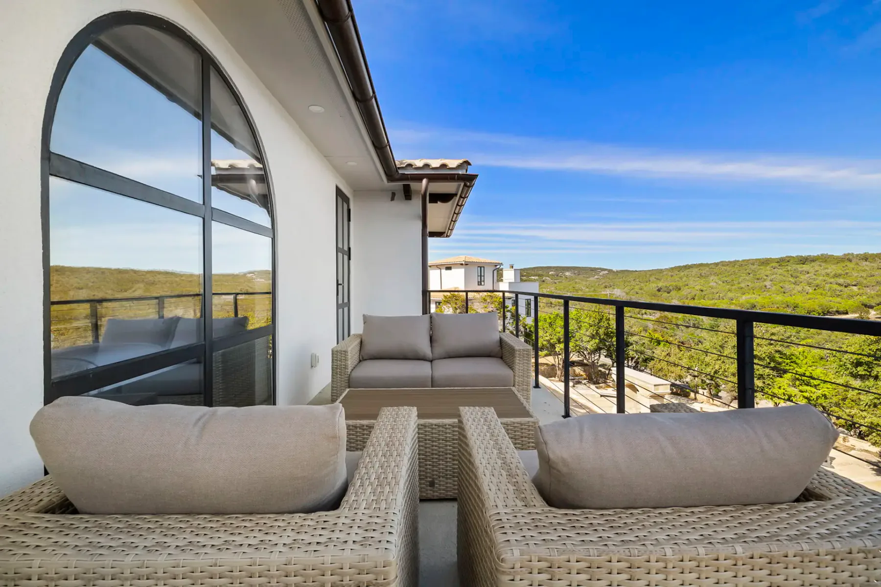 Outdoor patio with wicker furniture set, including two armchairs and a sofa, overlooking green hills under a clear blue sky.