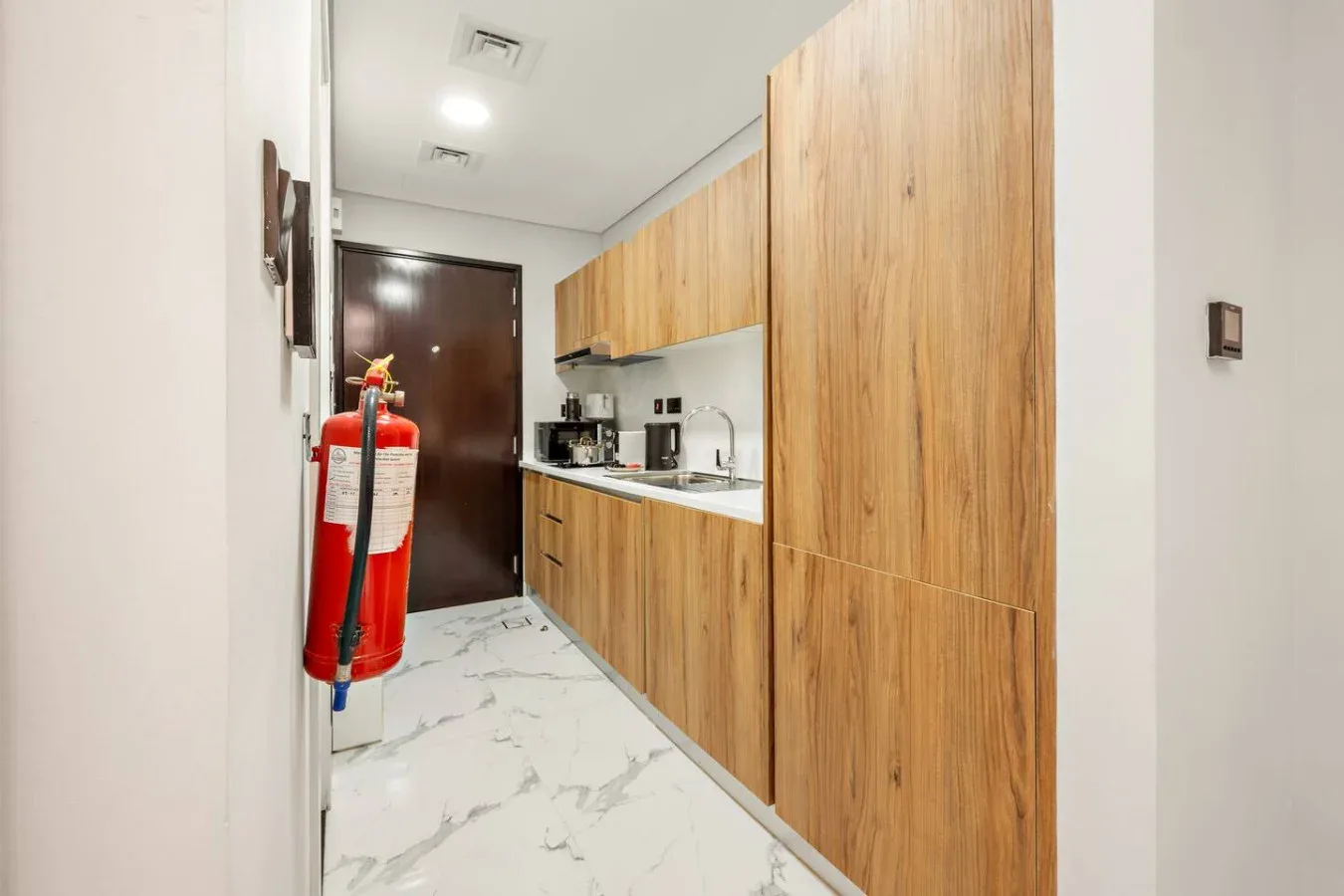 Una pequeña cocina con gabinetes de madera, una encimera y una puerta oscura al fondo.