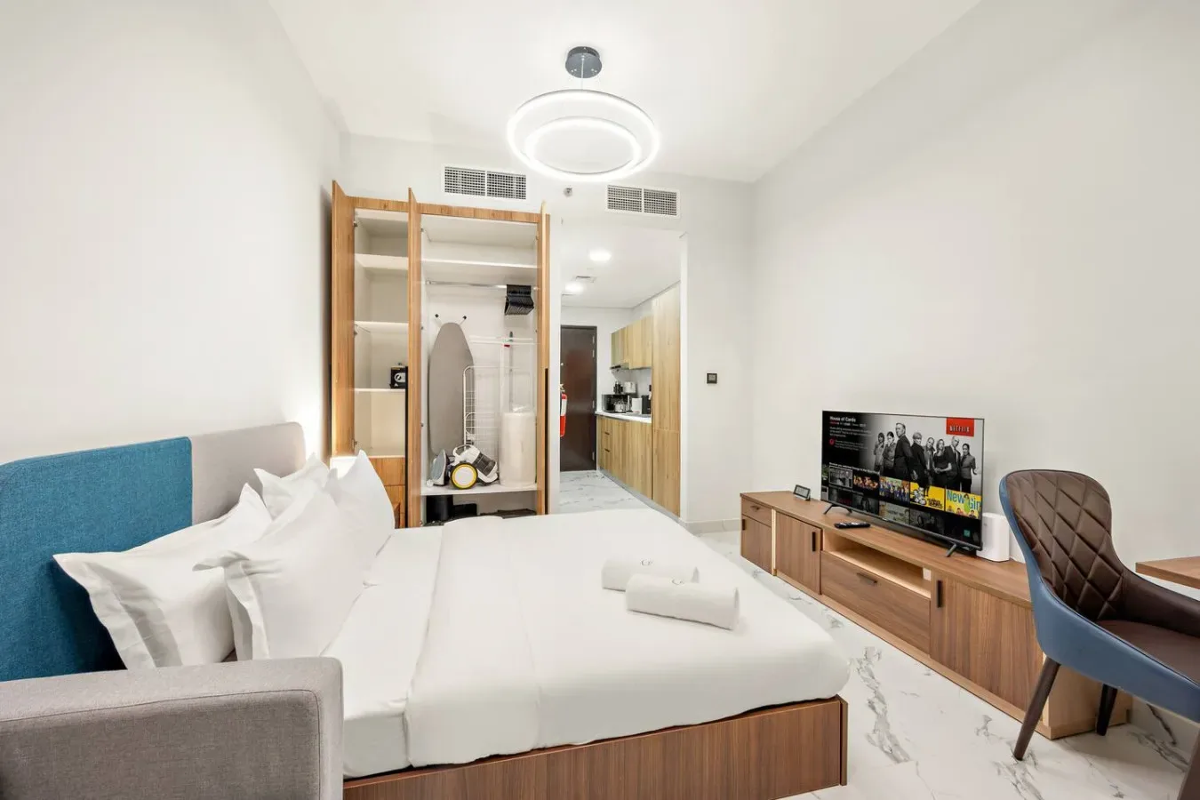 Un dormitorio luminoso con una cama grande, armario abierto y televisor.