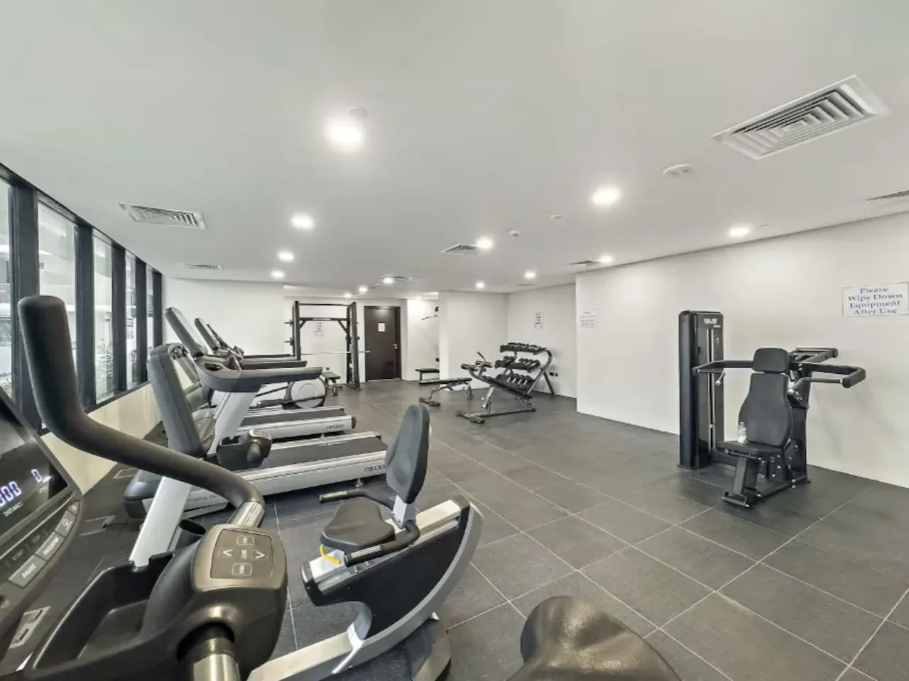 A spacious fitness room with exercise machines arranged along the windows.