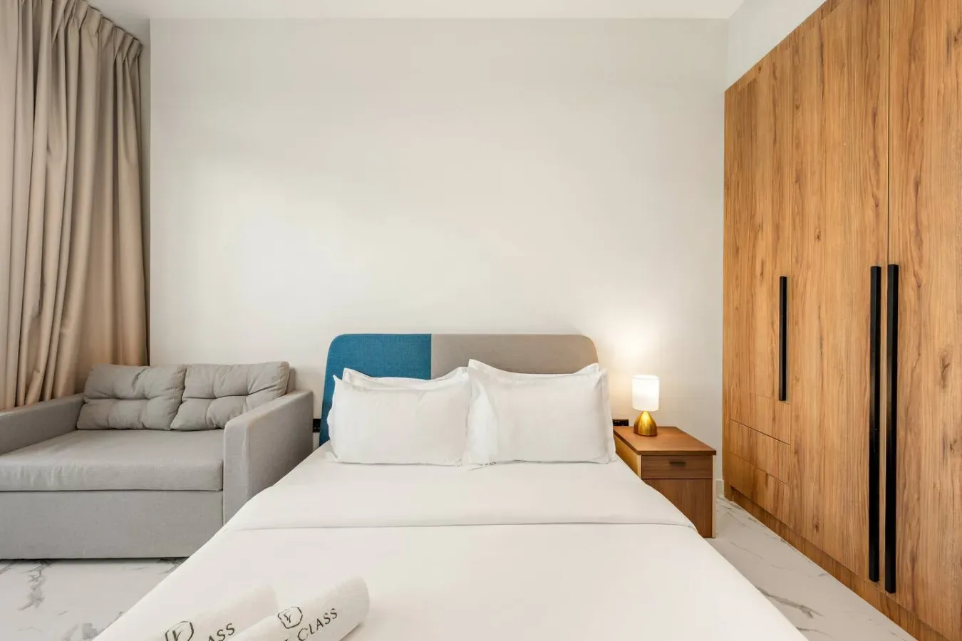 Un dormitorio con una cama, una zona de estar gris y un armario de madera.