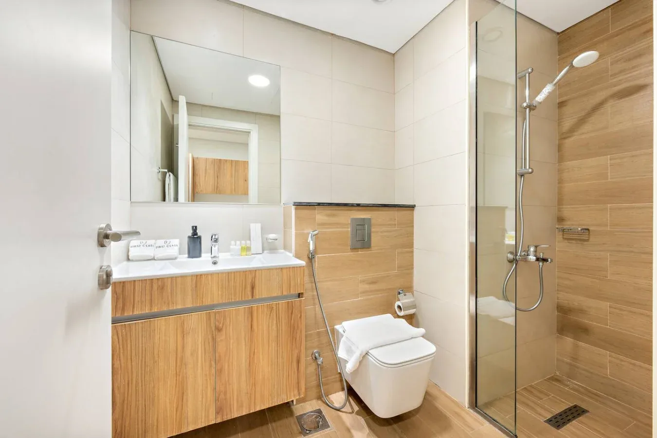 Un baño moderno con mueble de acabado madera y ducha con mampara de vidrio.