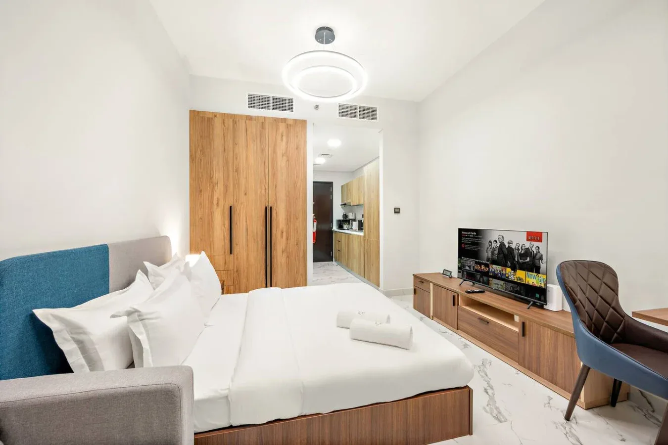 Un dormitorio luminoso con una cama tendida y un televisor sobre un mueble bajo.