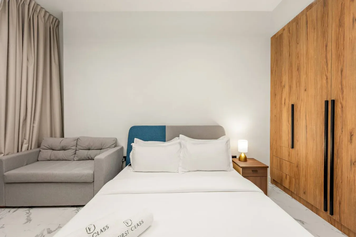Dormitorio con una cama bien hecha, una zona de asientos gris y armarios de madera.