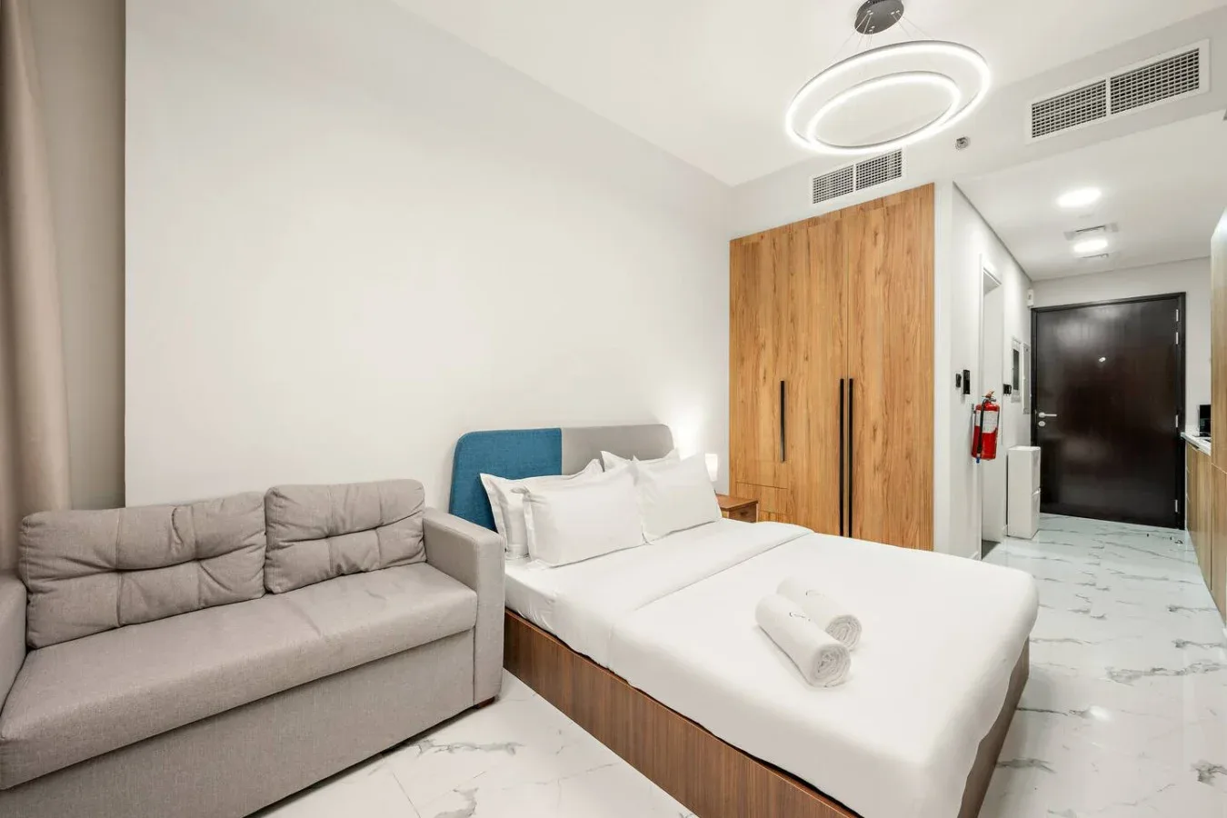 Un dormitorio con una cama tendida junto a un sofá y un armario de madera.