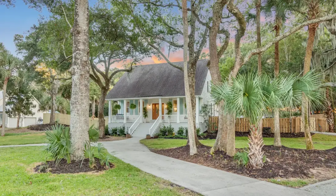 A cottage-style house with a covered porch sits among trees beside a curved walkway.