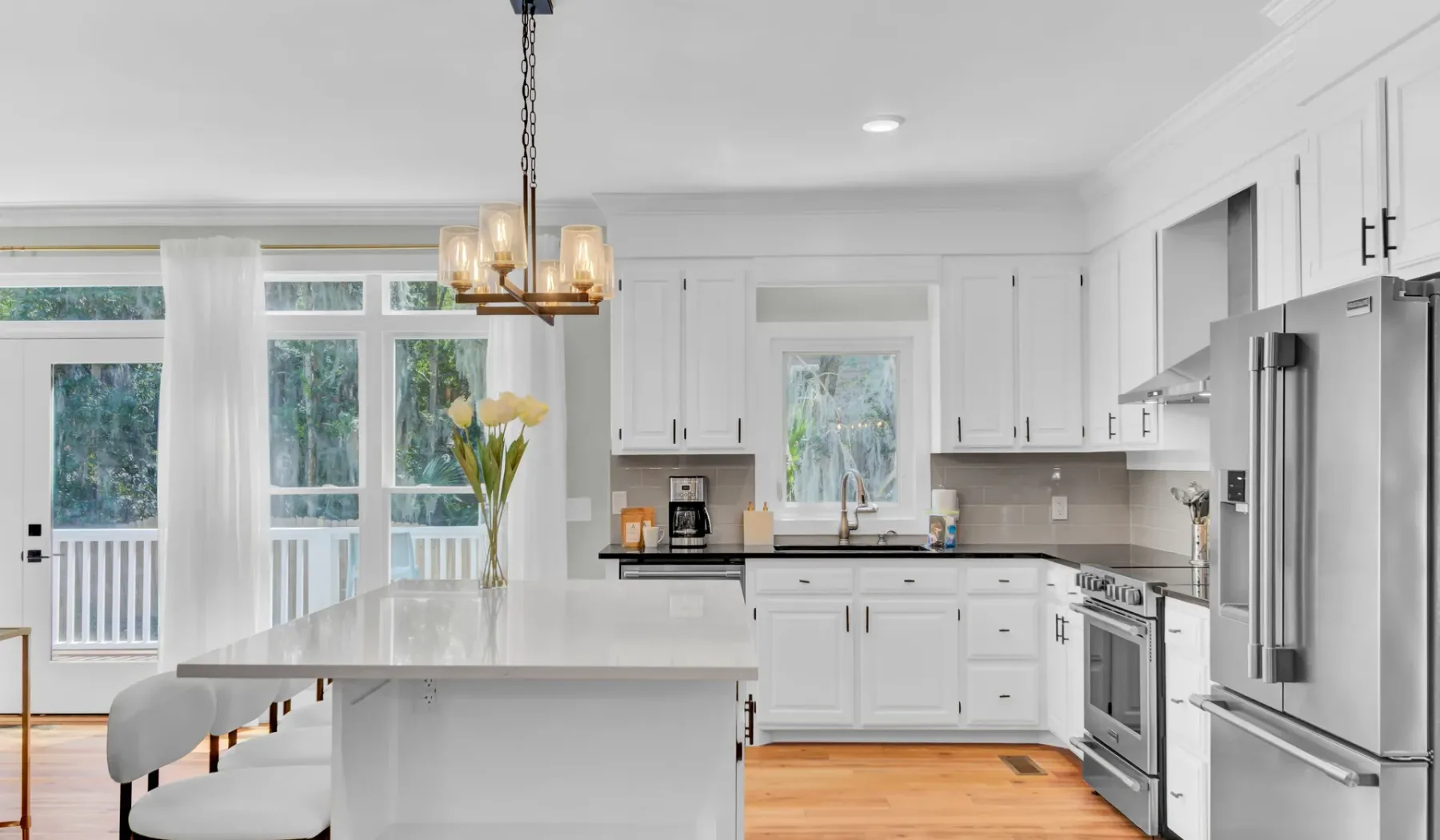 A bright kitchen with white cabinetry, a central island, and large windows.