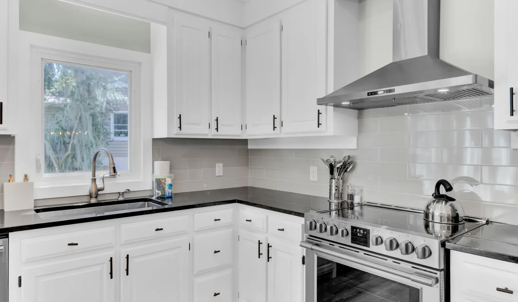 A bright kitchen with white cabinets, dark counters, and a stainless steel range.