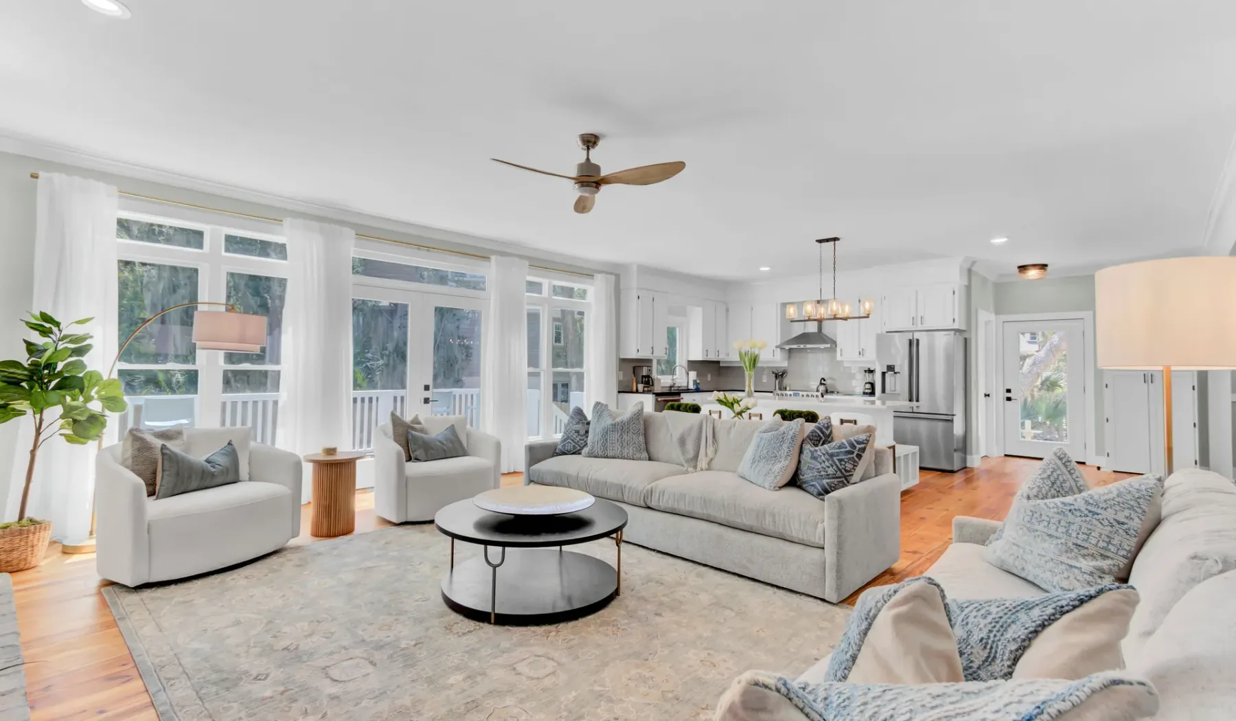 A bright open-plan living room with seating and a kitchen in the background.