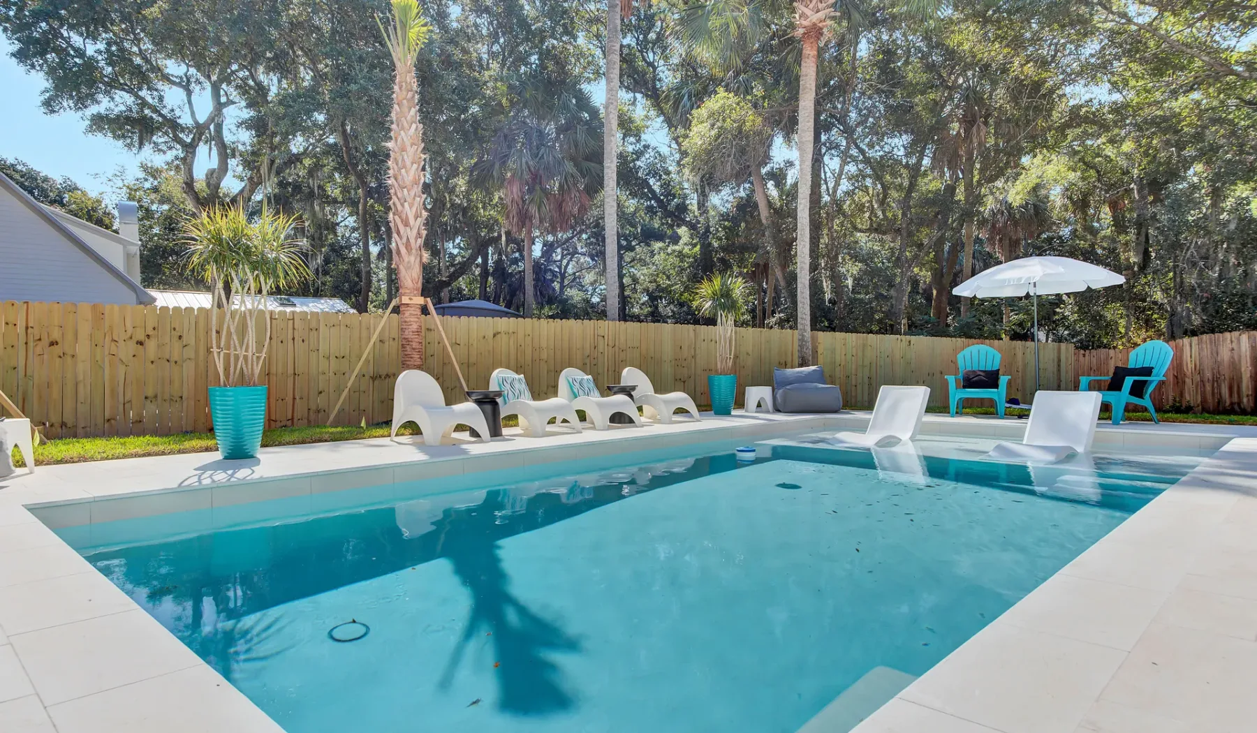 An outdoor swimming pool is surrounded by lounge seating and a wooden fence.