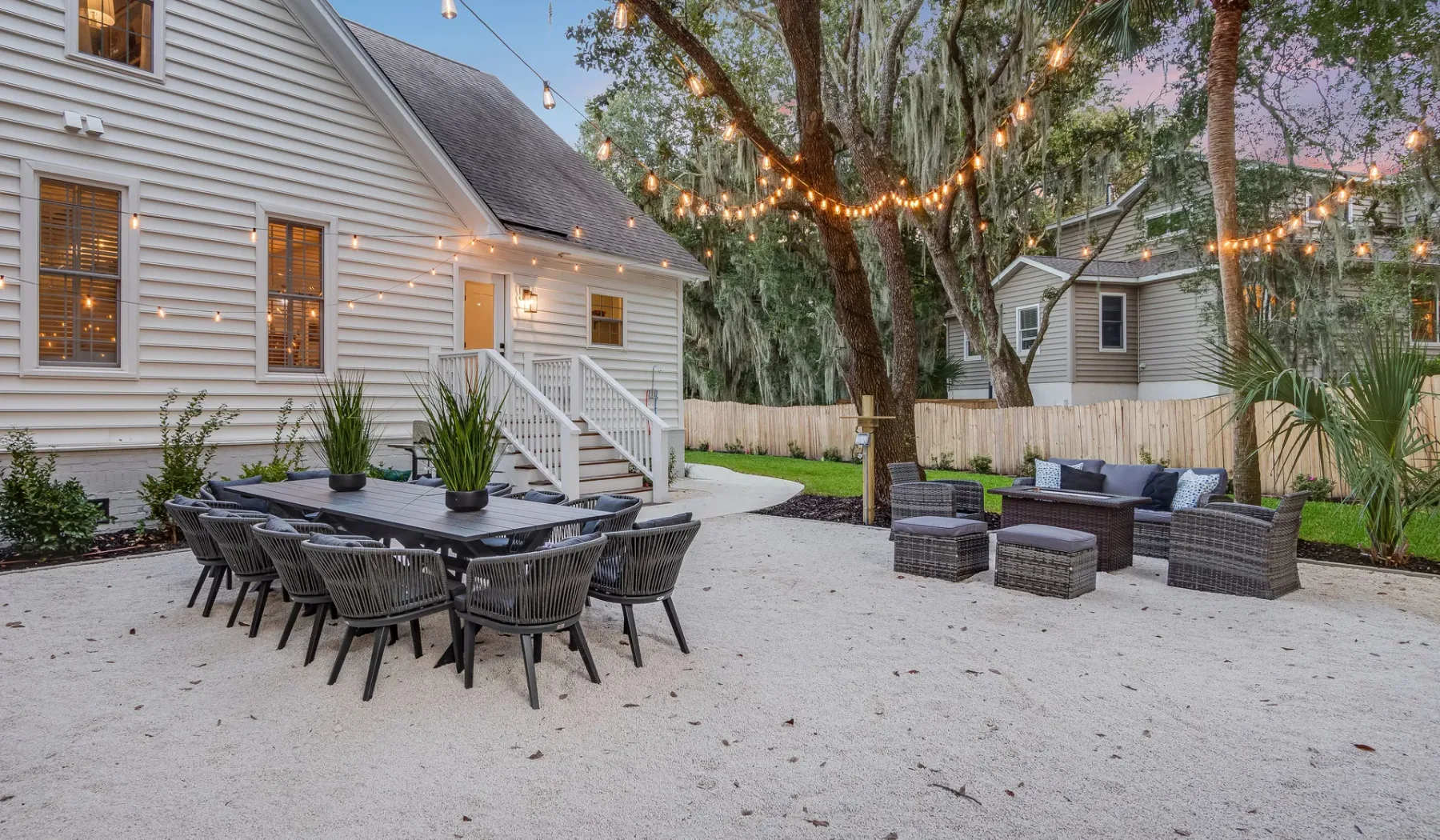 An outdoor patio with a dining table and lounge seating beneath string lights.