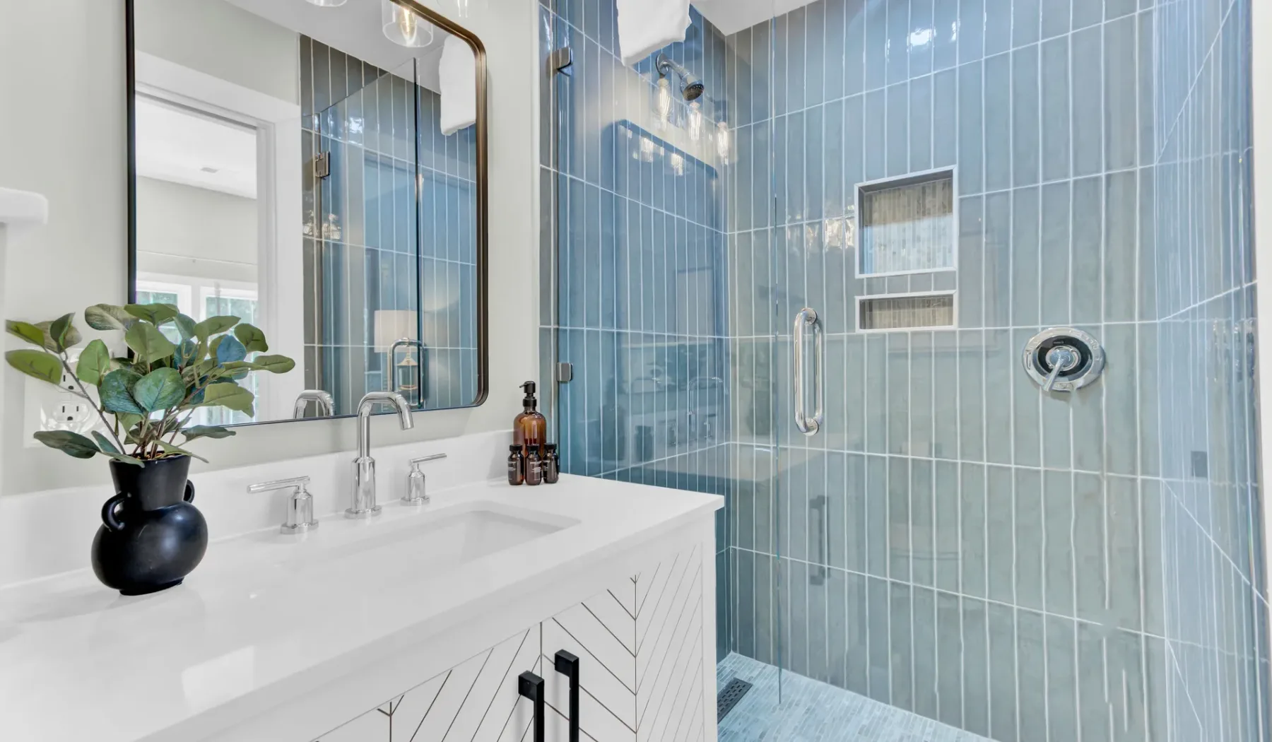 A bathroom vanity stands beside a glass shower with blue tile.
